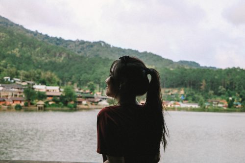 一位綁馬尾的女子面向湖景的背影，女子微笑
