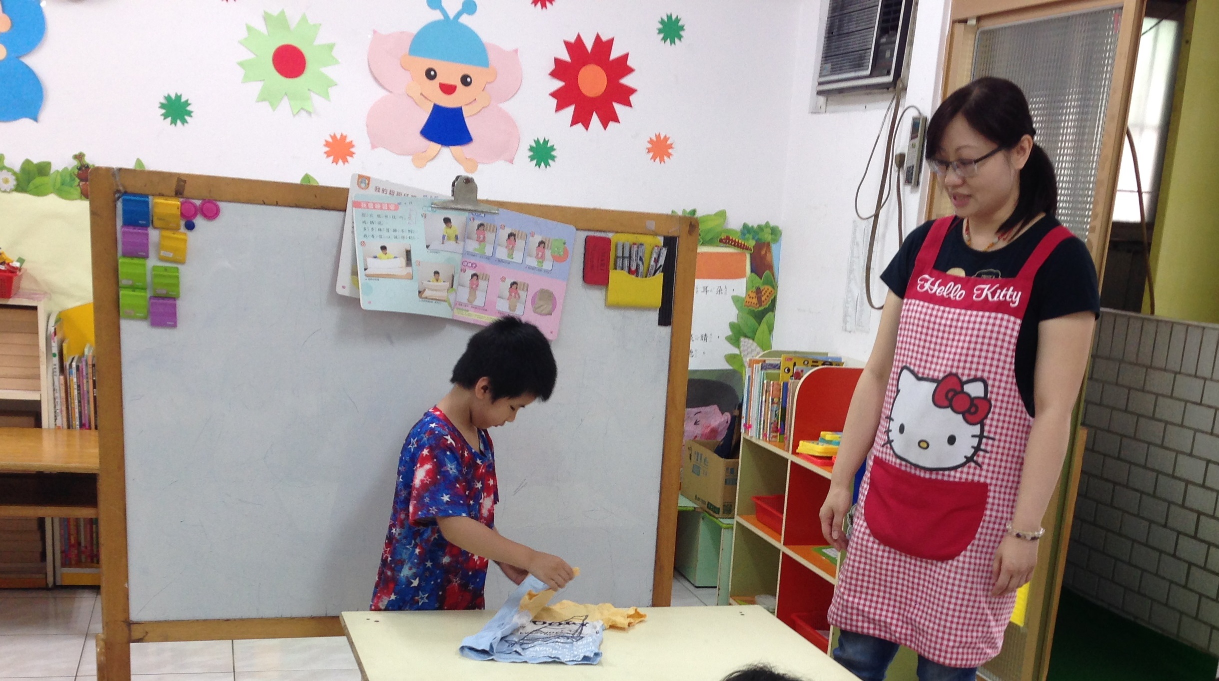 教室裏一位女性教室站在照片右方，左方則為一個小孩正在操作桌上教材