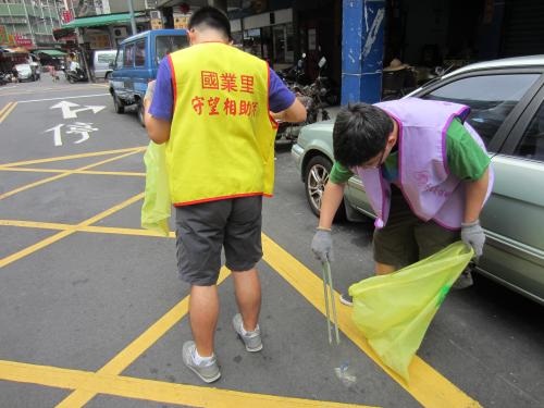 照片中有2固人穿著背心在馬路旁做清潔工作，其中一人彎腰