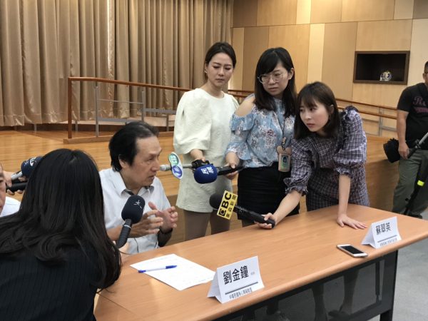 劉金鐘坐在椅子上，前方有一桌卓，左側有3位記者，右則有一位記者，各記者手持麥克風採訪。