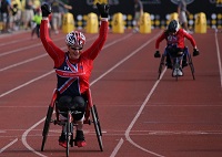 跑道上有一位女性的競速輪椅參賽者高舉雙手一臉喜悅狀