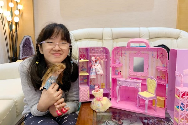 作者女兒在客廳的照片，身旁矮桌上放置粉紅色組的娃娃屋