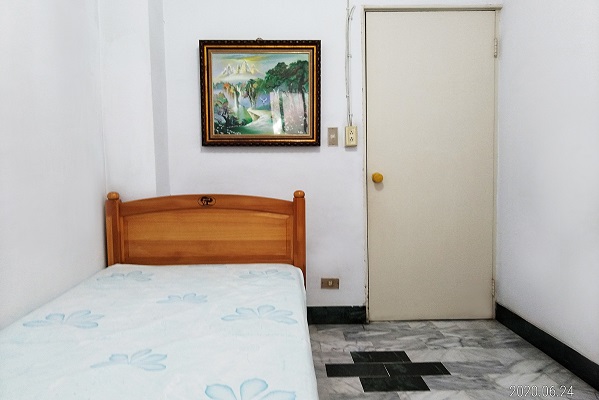 房間裏有一張單人床，牆上有一富畫，左側則為房門。