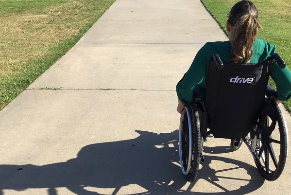 一位長髮女性身著綠色夾克，坐輪椅者的背影