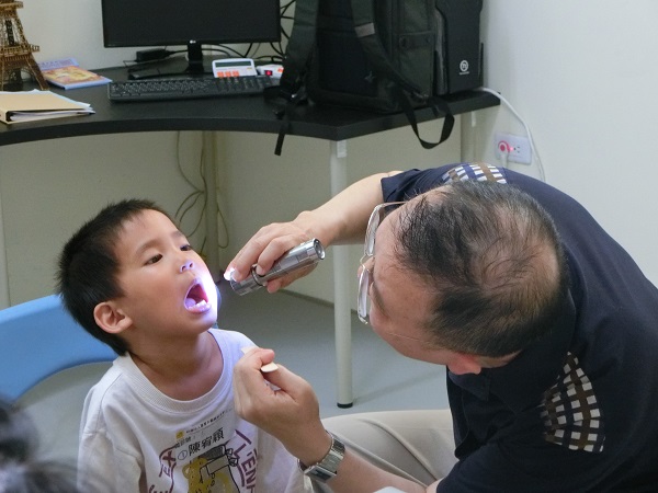 一位醫生拿手電筒照著小男孩子嘴裏