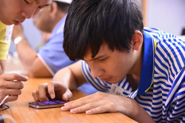 一位年輕男性低頭使用放在桌上的手機