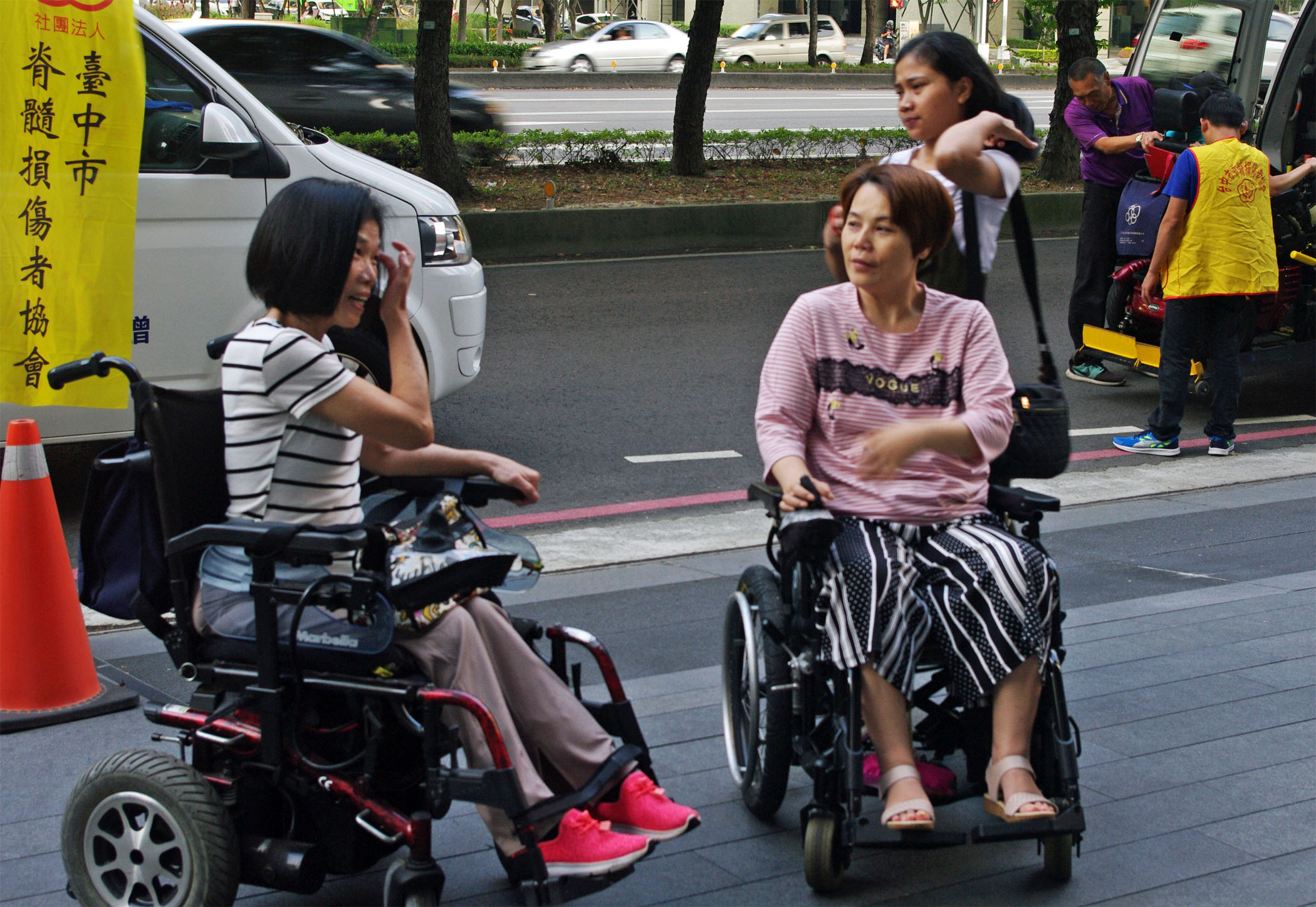 作者與其他傷友一起參與協會活動，二者皆坐在輪椅上於馬路邊稍做等待。