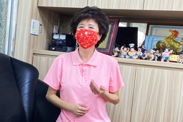 中華民國聲暉聯合會理事長莫素娟身穿粉紅色polo衫，口戴紅色口罩，坐在沙發上微笑面對鏡頭。